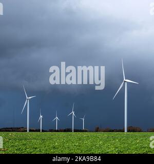 dark threatening grey sky and white wind turbines in belgium Stock Photo