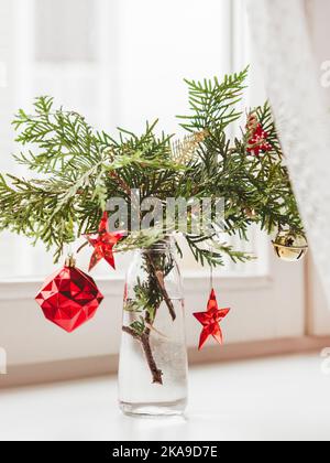 Vase with decorated thuja branches stands on window sill. Sustainable alternative for Christmas tree. Caring for nature. Refusal to cut down spruce fo Stock Photo