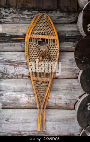 Pair of traditional vintage wooden-framed, rawhide-latticed snowshoes hanging on outer wall of log cabin Stock Photo