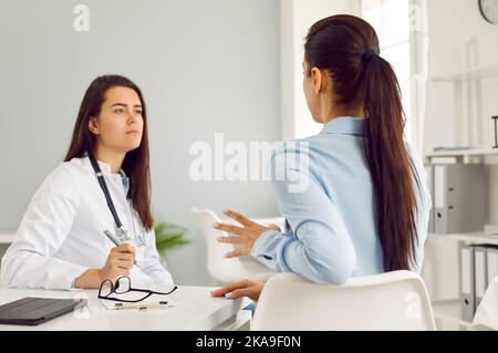 Young Caucasian woman in doctor coat looks and female patient during consultation at medical hospital Stock Photo