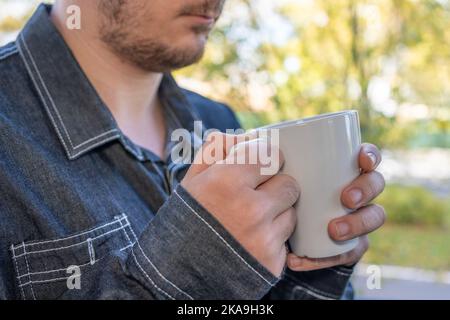 man's hand holding a cup of coffee next to a window with autumn background outside Stock Photo