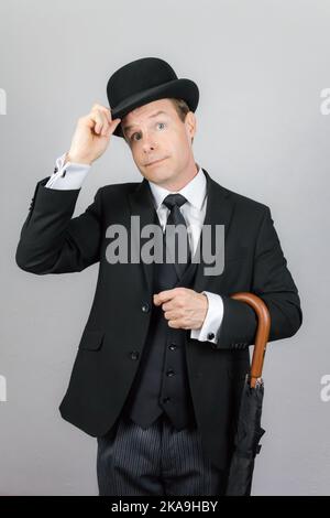 Portrait of British Butler in Dark Suit and Umbrella Tipping Bowler Hat. Vintage Style and Elegant Courtesy. Stock Photo