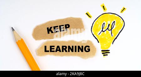 Business and finance concept. A lamp is drawn on a white sheet, there is a pencil and scraps of paper on which it is written - KEEP LEARNING Stock Photo