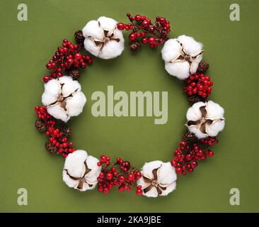 green background with a Christmas wreath from red berries and flowers of cotton Stock Photo