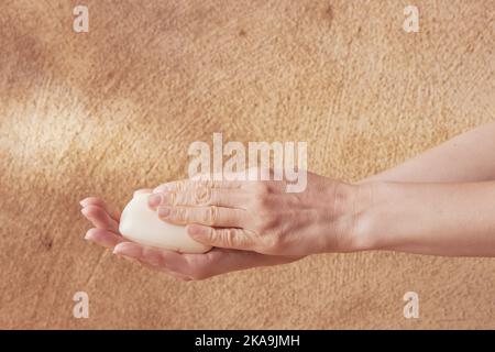 A young woman touching a soap with her hands on a beige background for spa advertising Stock Photo