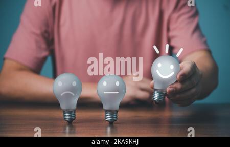 Customer service satisfaction concept, Young businessman holding happy face light bulb, smile satisfaction rating icon face. Stock Photo