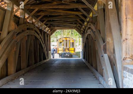 Installing a New Yellow Passenger Antique Coach Thru a Cover Bridge on to a Railroad Track on a Fall Day Stock Photo