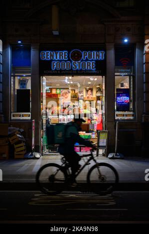 LONDON - November 3, 2020: Centre Point Food Store entrance at night with motion blurred silhouette of delivery cyclist in passing in front Stock Photo