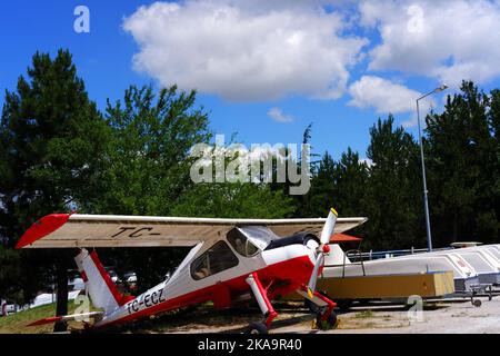White plane parked within trees in a sunny day outdoor with cloudy sky Stock Photo