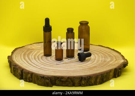 Mockup of brown glass vials with dropper lid on wooden board and on yellow background. Empty glass bottles of different sizes and pipette. Concept of Stock Photo