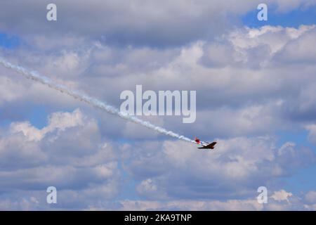 Plane flying within dark clouds with smoke on tail Stock Photo
