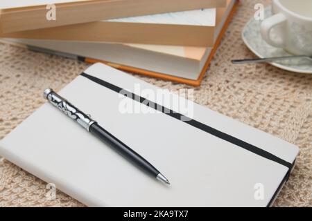 Pen on a notebook next to some books and a cup of coffee on a table Stock Photo