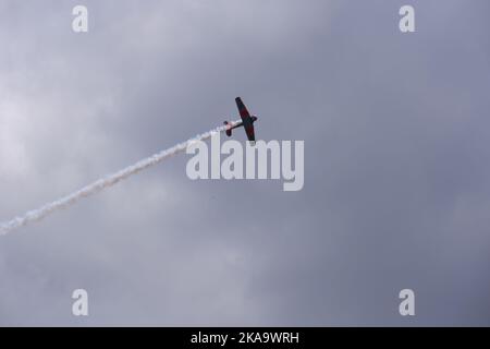 Plane flying within dark clouds with smoke on tail Stock Photo