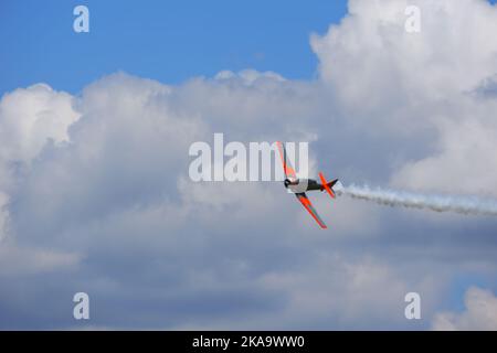 Plane flying within dark clouds with smoke on tail Stock Photo
