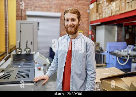 Waist up portrait of smiling young man working in industrial printing shop and looking at camera, copy space Stock Photo