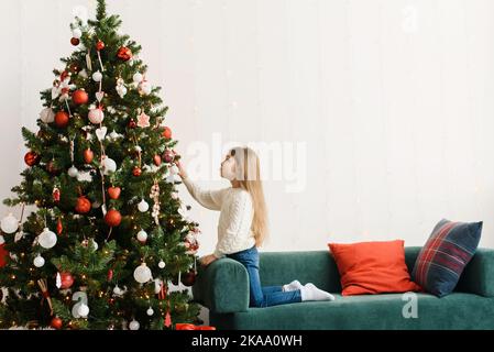 A cute little girl decorates the Christmas tree on Christmas morning Stock Photo