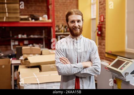 Waist up portrait of smiling young man working in industrial printing shop and standing with arms crossed, copy space Stock Photo