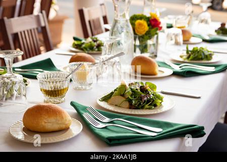 Fine dining table setting; plated salad, dinner rolls and various dressings with various plates and silverware. Stock Photo