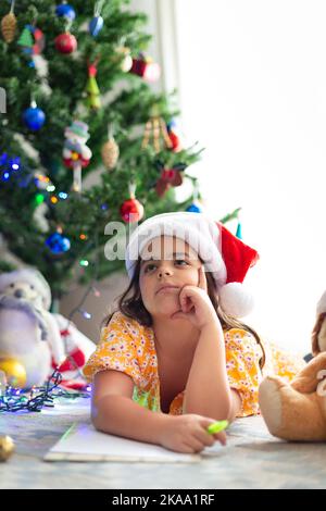 Caucasian little child thinking to write her wish list to Santa Claus. Christmas time. Space for text. Stock Photo