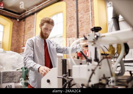 Portrait of young man working in print shop and operating industrial printing machine, copy space Stock Photo