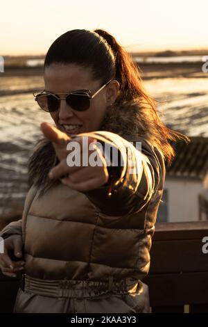 Portrait of young caucasian woman in gold coat and sunglasses pointing finger at camera. Lifestyle concept Stock Photo
