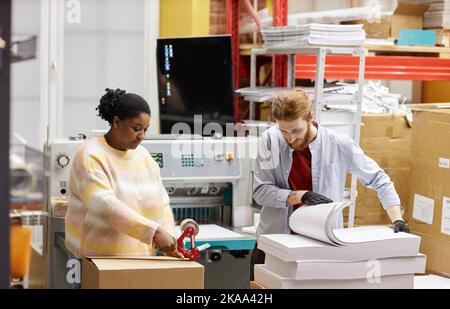 Portrait of two workers opening boxes with paper in industrial print shop, copy space Stock Photo