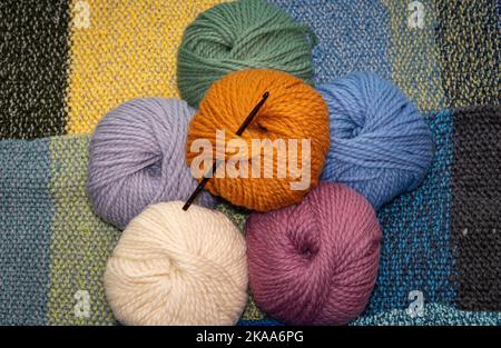 Wool yarn balls of various colors with crochet needle, thick wool for knitting and crochet against knitted background Stock Photo