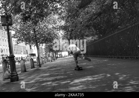 A greyscale back view of a young male skateboarding in the St. Stephen's Green park in Dublin, Ireland Stock Photo