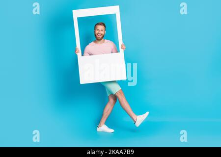 Full size photo of handsome young guy cheerful walking model window frame dressed stylish pink look isolated on aquamarine color background Stock Photo