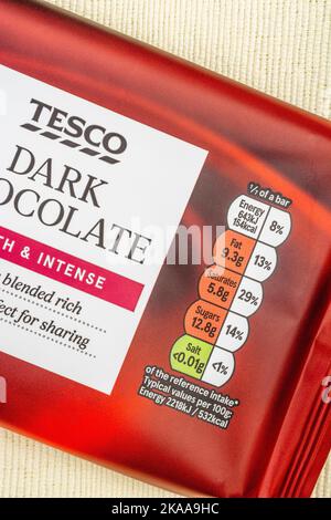 Close-up Tesco brand dark chocolate soft plastic film food packaging with dietary nutrition traffic light box with food fat content & high in sugar. Stock Photo