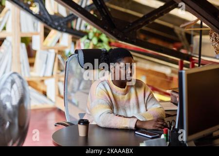 Portrait of young black woman using computer at workplace in printing shop or publishing company, copy space Stock Photo