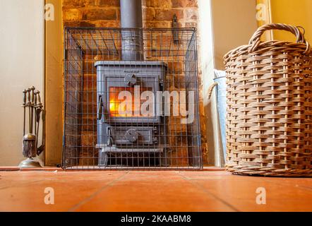 Flaming log wood burning stove behind a mesh fire guard in one of the National trusts rock cottages on Kinver Edge Staffordshire England Stock Photo