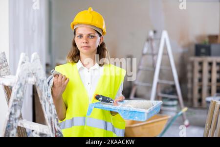 Woman builder holding paint roller and tray, home improvement works Stock Photo