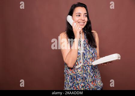 Smiling indian woman talking on landline phone, customer support service. Cheerful lady chatting, holding retro telephone, person with positive facial expression answering call Stock Photo
