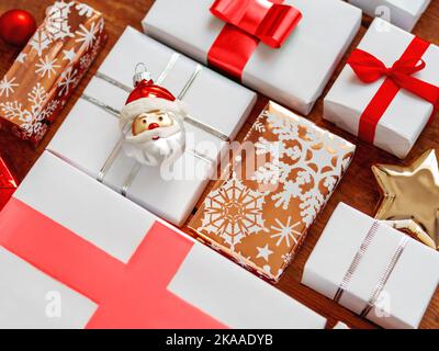 Christmas presents on shabby wooden background. New Year gifts in white and golden paper with bright red ribbons. Santa Claus decoration. Stock Photo