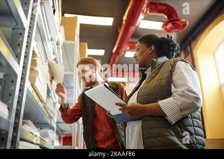 Low angle view at two workers taking stock of production at print factory warehouse Stock Photo