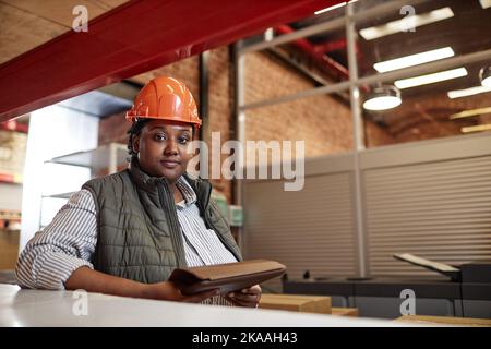Portrait of African American woman wearing hardhat in factory warehouse and looking at camera Stock Photo