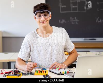 Young male technology student looking at camera with protective glasses in electronics class Stock Photo