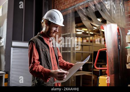 Side view portrait of bearded worker wearing hardhatat factory and looking at documents Stock Photo