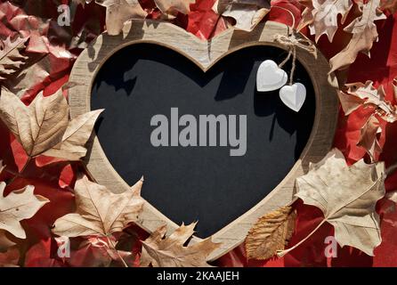 Heart shaped letter board, blackboard with heart trinkets. Dry Autumn leaves, natural Fall decor on crumpled red paper background. Copy-space, place Stock Photo