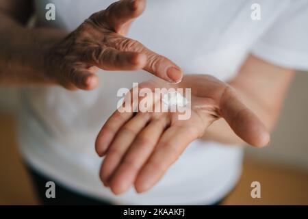 Selective focusing moisturising lotion cream on senior woman hands. Closeup portrait. Beauty treatment. Skin care. Medical healthcare. Stock Photo