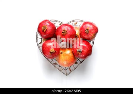 Many pomegranates in a heart-shaped basket. on white background. Stock Photo