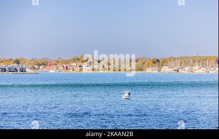Small boat with people fishing and Greenport in the distance Stock Photo