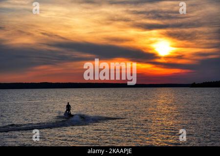 Jet skier driving off into the sunset on a summer night Stock Photo