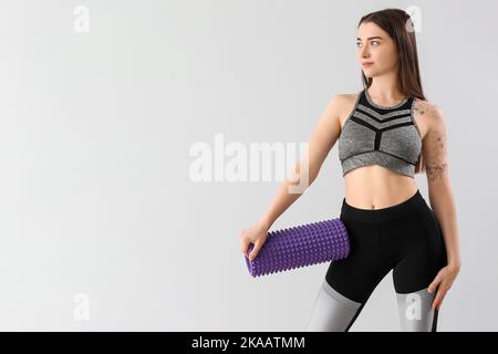 Sporty young woman with foam roller on light background Stock Photo