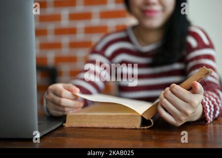 Smart and pretty young Asian female college student researching informations on textbook, reading a book in the campus library. cropped image Stock Photo