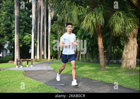 Handsome sporty Asian man in sportswear running or jogging in the beautiful city park. Athletic, Fit, Healthy lifestyle Stock Photo