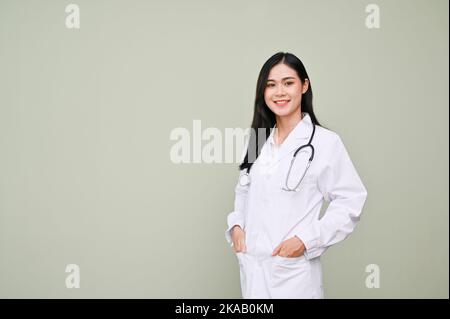Professional and beautiful Asian female doctor in uniform with stethoscope standing against grey background with copy space for text. Stock Photo