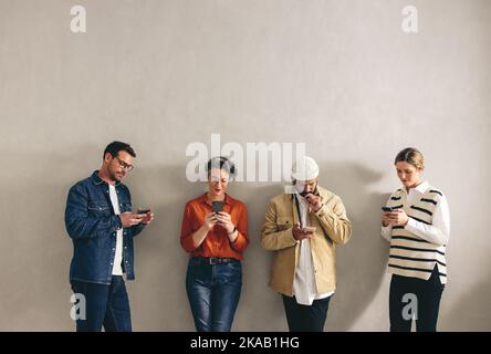 Diverse businesspeople using their smartphone while standing in line in a waiting area. Group of shortlisted candidates browsing the internet before a Stock Photo
