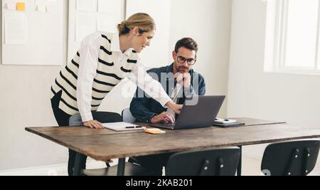 Two business colleagues having a discussion while working with a laptop in a creative office. Two businesspeople sharing ideas while working together Stock Photo
